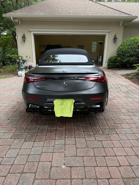 Black Mercedes-Benz sedan parked in driveway with neon yellow towing strap attached to rear