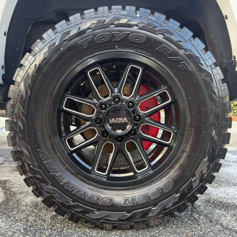 Black SUV tire with TOYO brand, red brake calipers visible, and decorative black and silver wheel rim