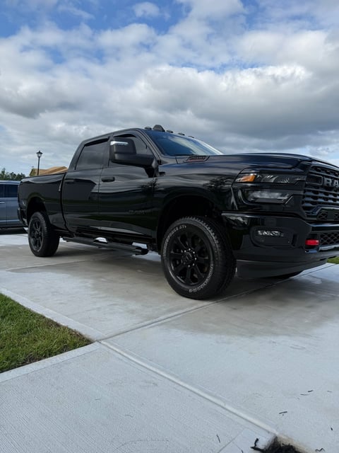 Black Ram pickup truck parked on a concrete driveway with cloudy blue sky in background
