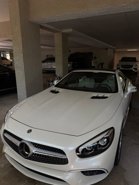 White Mercedes-Benz convertible parked in an indoor garage with concrete pillars and other vehicles visible in the background