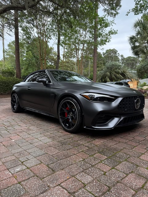 Black Mercedes-AMG sports coupe parked on brick driveway with trees in background