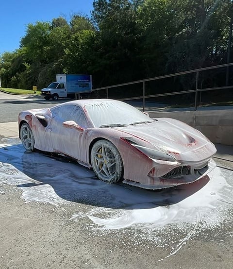 Red Ferrari covered in white foam and soapy water during outdoor car wash in parking lot