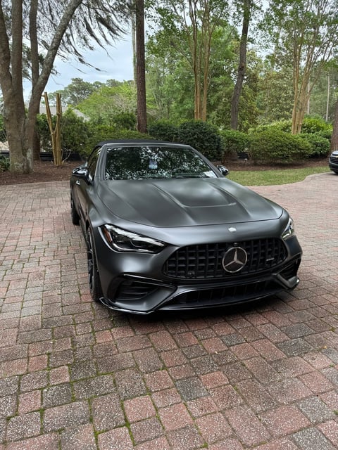 Black Mercedes-AMG sports car parked on brick driveway with trees in background
