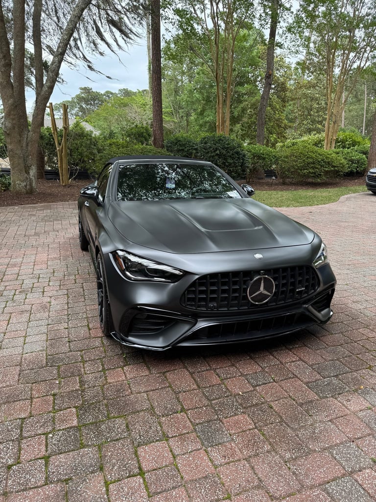 Black Mercedes-AMG sports car parked on brick driveway with trees in background