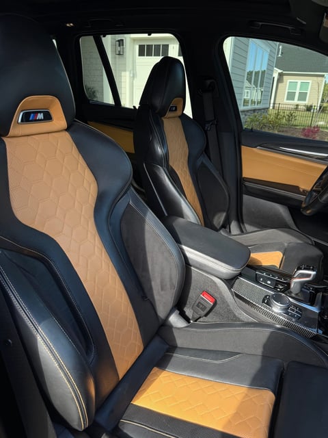 Car interior with black and tan leather sport seats, carbon fiber trim, and manual transmission shifter visible through the windows