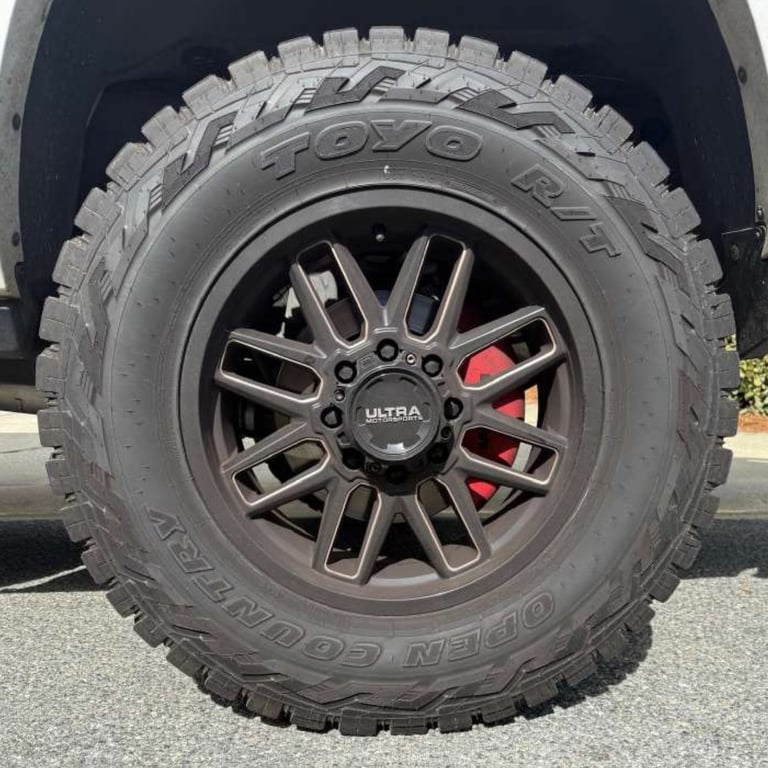 Close-up of a vehicle wheel with a dark multi-spoke rim and Toyo all-terrain tire with red brake caliper visible