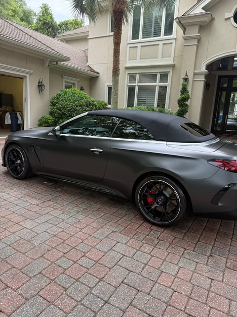 Gray sports coupe parked in driveway of modern home with palm tree and manicured landscaping