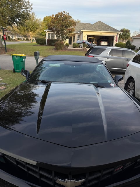 Black Chevrolet parked in suburban driveway with yellow trash bin, green bin, and house with open garage in background
