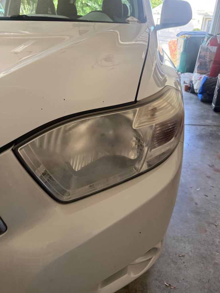 Close-up of a cloudy headlight on a white car parked in a driveway