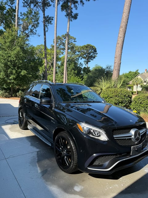 Black Mercedes-AMG SUV parked on driveway with tall pine trees in background