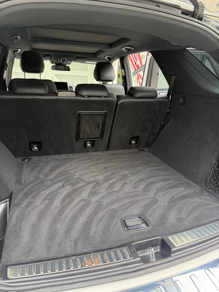 Empty car trunk with gray carpeted floor, black seats visible through windshield, parked indoors