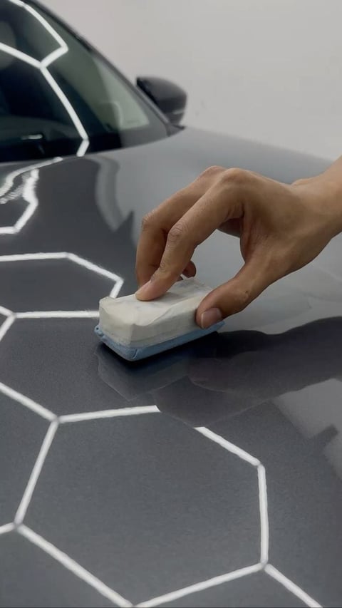 Hand applying ceramic coating to car hood with white hexagonal pattern protection layer visible