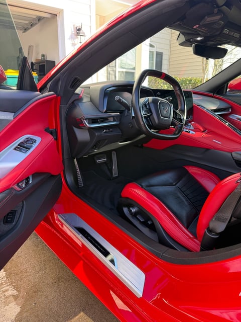 Interior view of a red sports car with black and red seats, steering wheel, and dashboard in a driveway