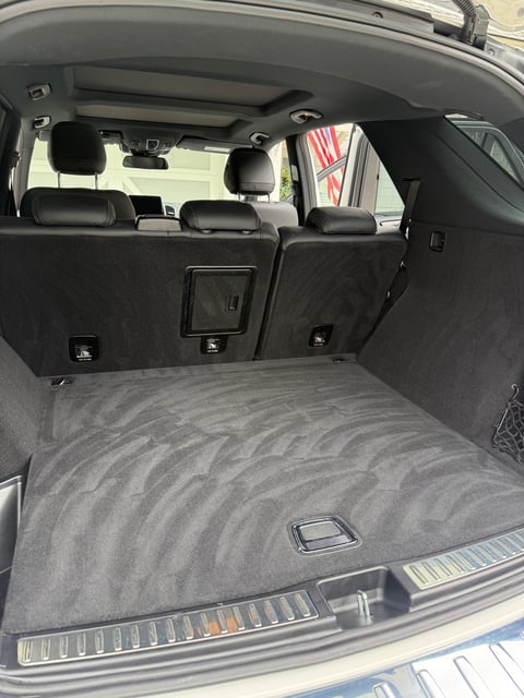 Interior view of a car trunk with gray carpeted floor, black seats visible in background, and control buttons on back panel